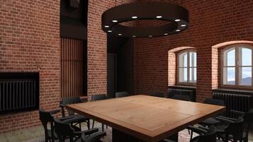 A spacious room with a large wooden table surrounded by chairs, brick walls, and arched windows.