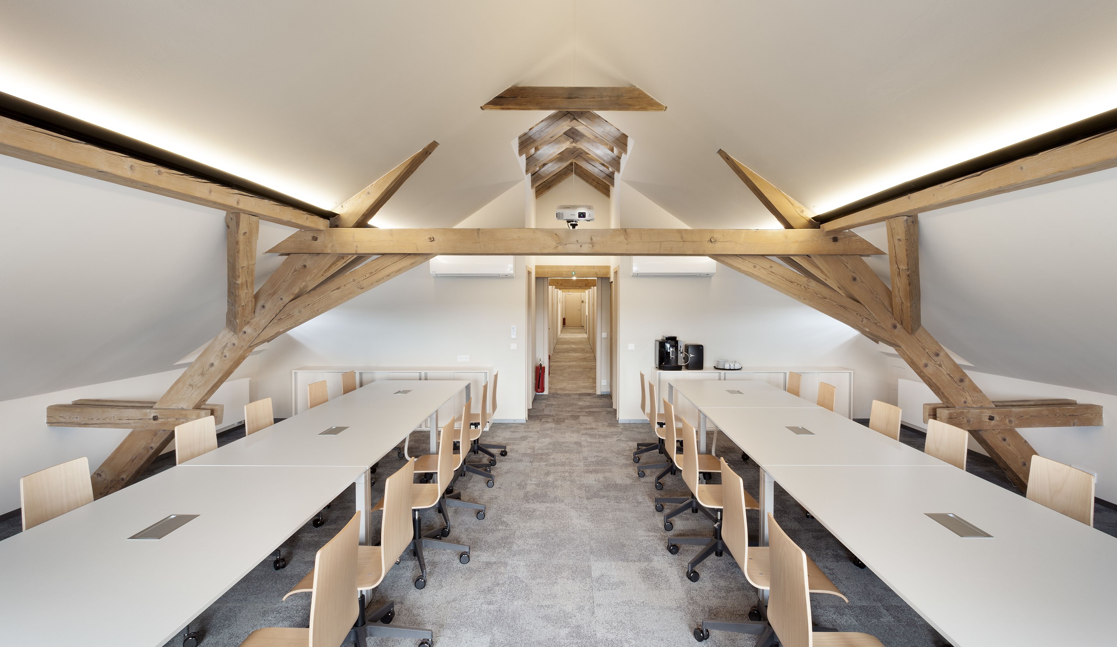 Un salón de conferencias con techo alto, vigas de madera a la vista y una larga mesa con sillas.