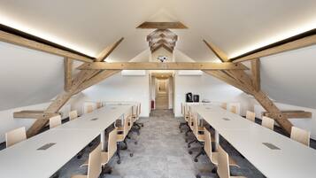 Un salón de conferencias con techo alto, vigas de madera a la vista y una larga mesa con sillas.