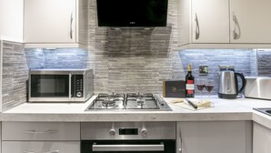 A modern kitchen with a built-in microwave, gas stove, and oven. There is a flat-screen TV mounted above the stove. - Forbes Retreat - Donnini Apartments (Ayr)