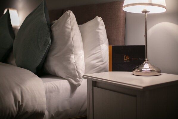 A neatly made bed with white bedding and a single green pillow, a bedside table with a lamp, and a black and orange sign on the wall. - Forbes Retreat - Donnini Apartments (Ayr)
