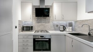 A modern kitchen with a flat-screen TV, microwave, gas stove, oven, and stainless steel sink. - Forbes Retreat - Donnini Apartments (Ayr)