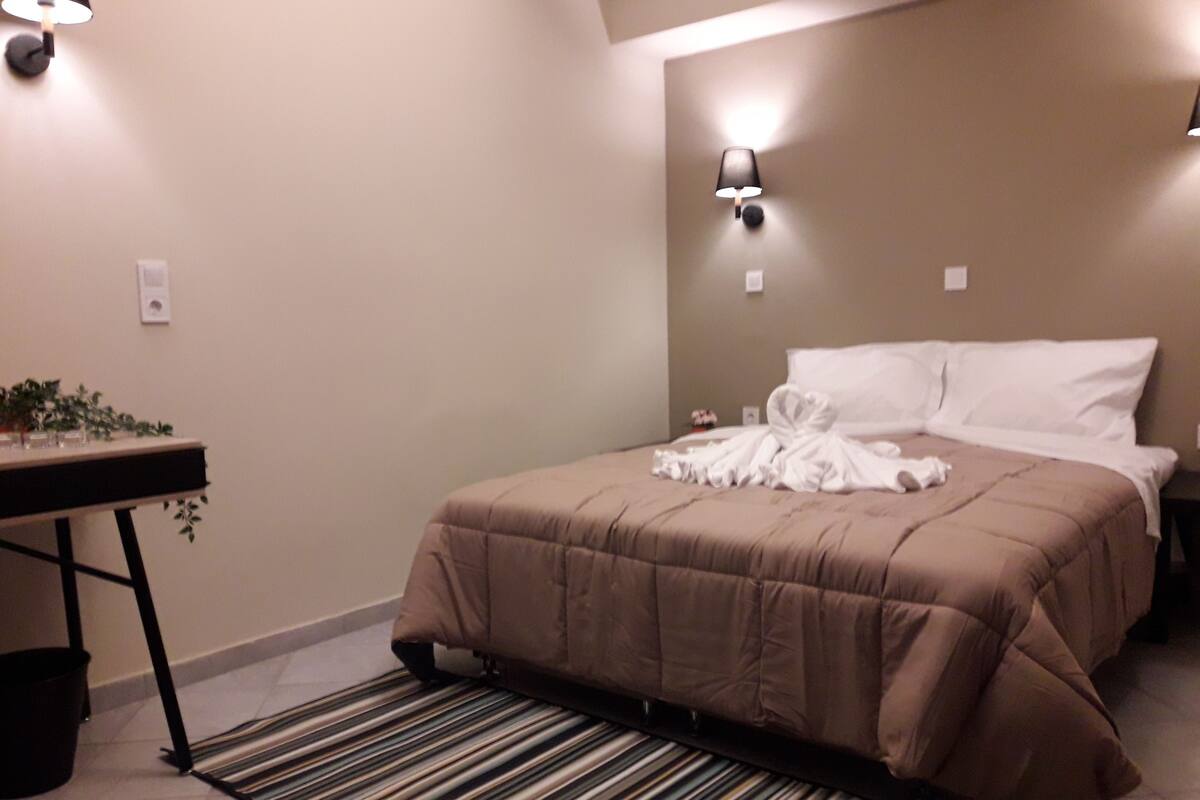 Hotellihuone, jossa on sänky, yöpöytä, lamppu ja raidallinen matto.