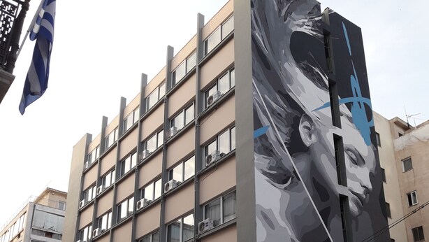 A multi-story building with a large mural on the side, air conditioning units on the facade, and a visible storefront with a sign.