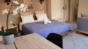 A hotel room with a bed, bedside tables, a desk, a chair, and a potted plant.
