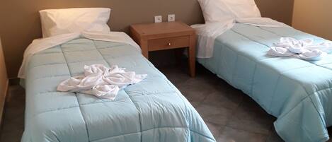 Two single beds with light blue bedding and white pillows, a wooden nightstand between them, and wall-mounted light fixtures.