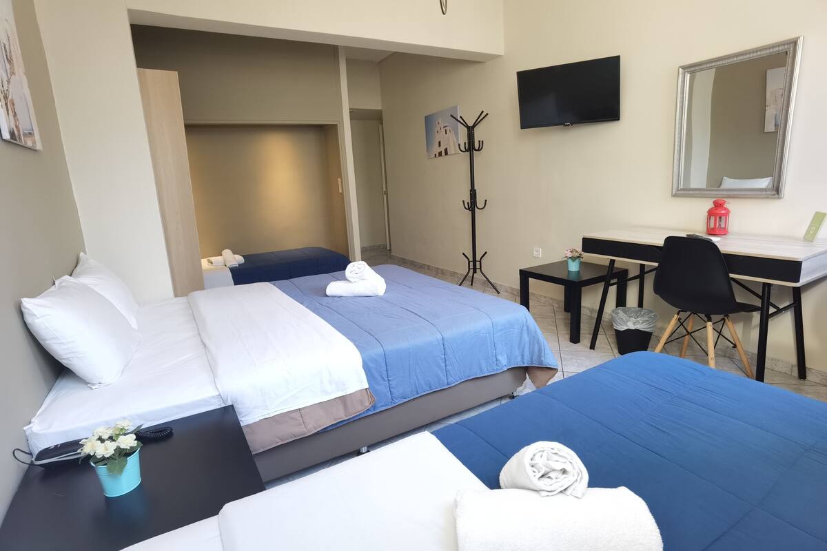 Hotellihuone, jossa on kaksi sänkyä, työpöytä, tuoli, televisio ja naulakko.