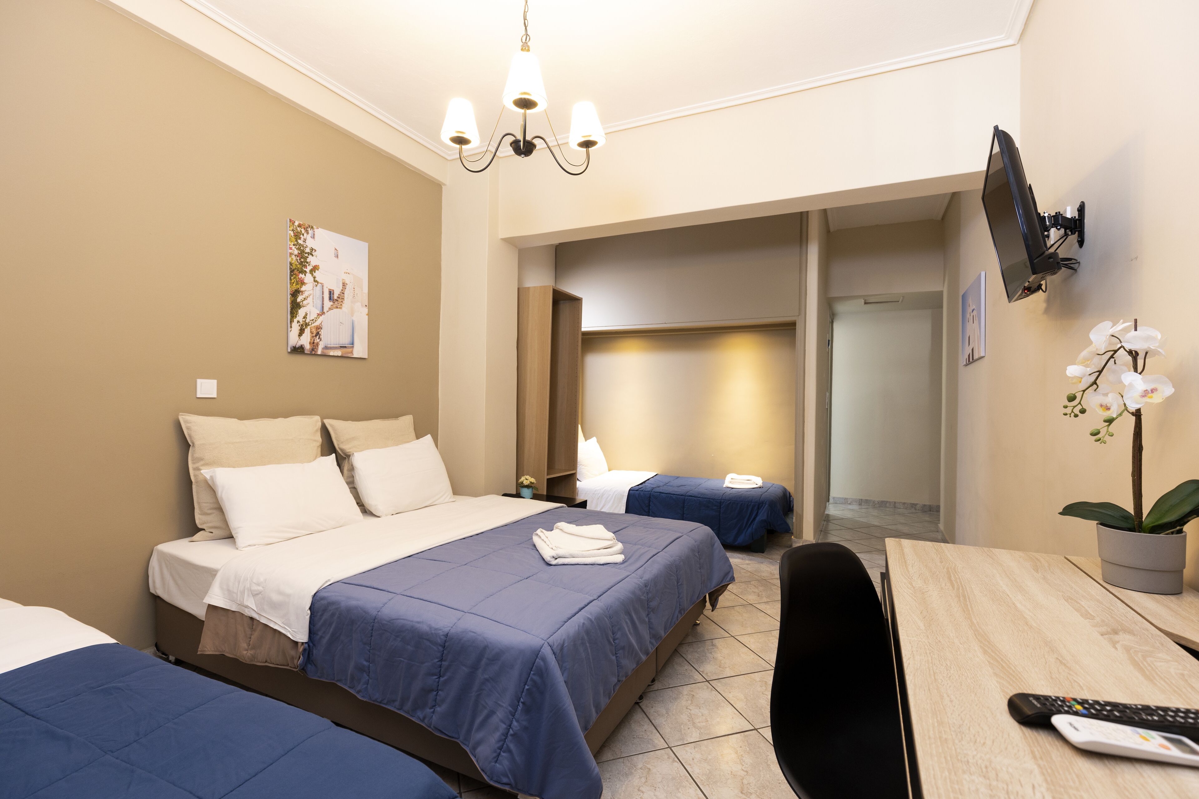 Een hotelkamer met een groot bed, twee kleinere bedden, een bureau en een aan de muur bevestigde televisie.