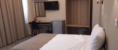 A hotel room with a bed, a desk, a chair, a wardrobe, and a TV.