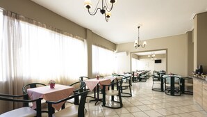 A dining area with multiple tables and chairs, a kitchen area, and a large window with curtains.