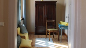 Een kamer met houten vloer, een donkere houten kast, een stoel, een tafeltje en een hanglamp.