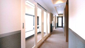 Un pasillo con puertas correderas de vidrio que dan a habitaciones, suelo alfombrado e iluminación empotrada en el techo.