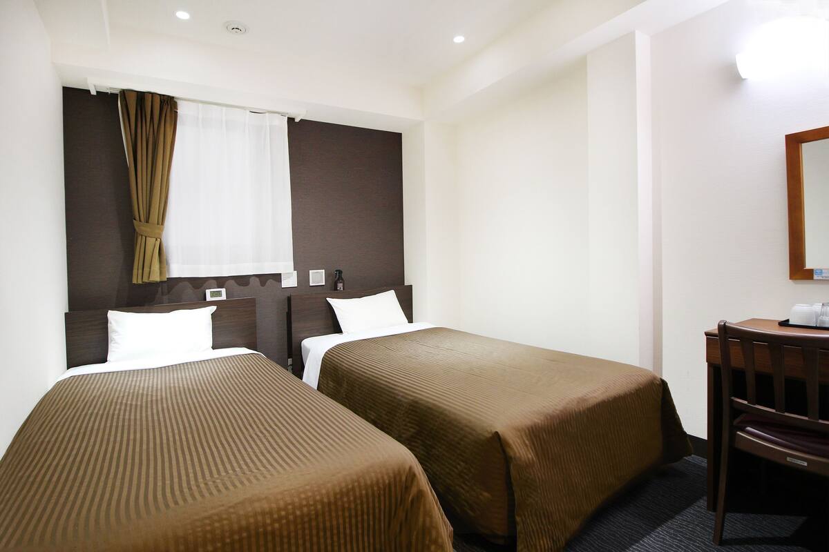 A hotel room with two single beds, a desk, and a chair.