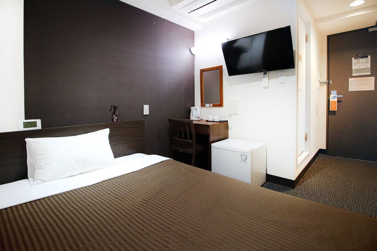 A hotel room with a bed, a desk, a television, and a small refrigerator.