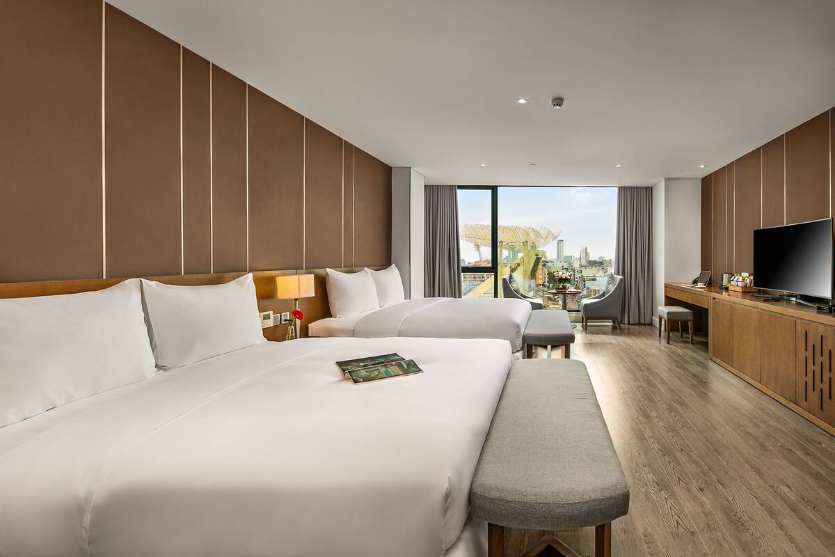 A hotel room with two beds, a TV, a desk, and a view of the city.