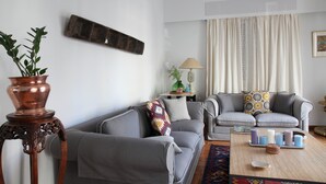 A living room with two grey sofas, a wooden side table with a lamp, a potted plant, and a coffee table with candles. - Stylish flat by the beach of Edem (Palaio Faliro)
