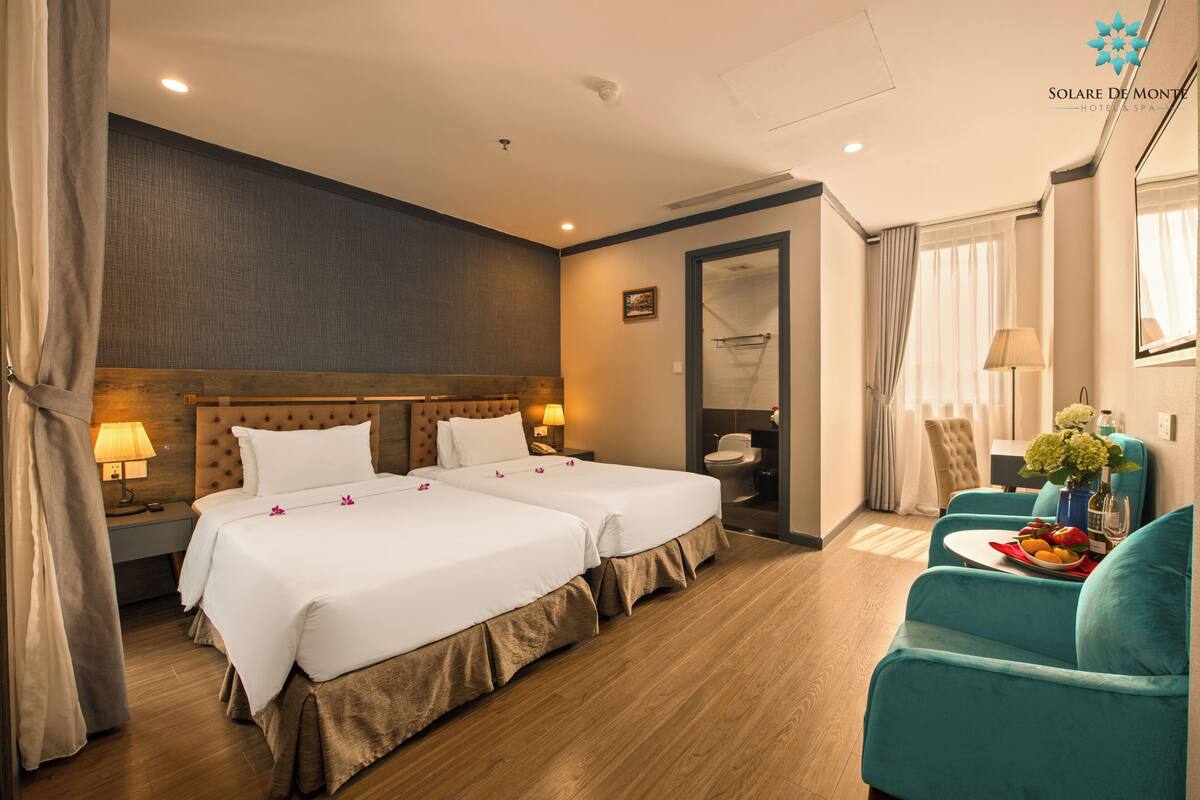 A hotel room with two beds, a sitting area with a table, and a bathroom visible through an open door.
