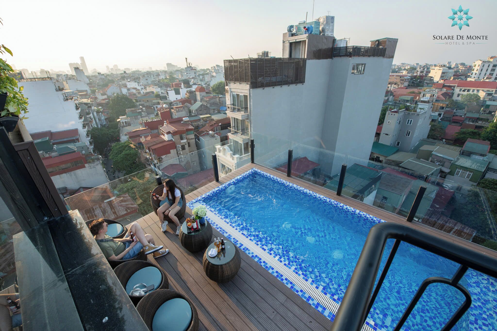A rooftop pool with clear views of the cityscape, surrounded by lounge chairs and a glass balustrade.