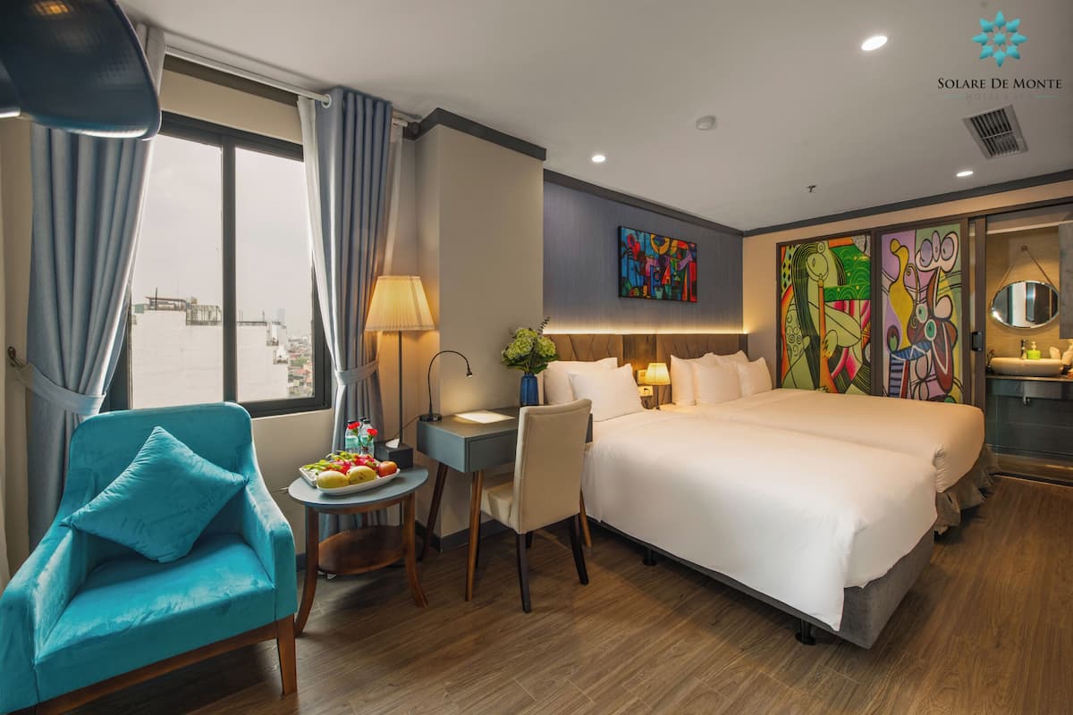 A hotel room with a large bed, a desk, a chair, and a view of the city through the window.