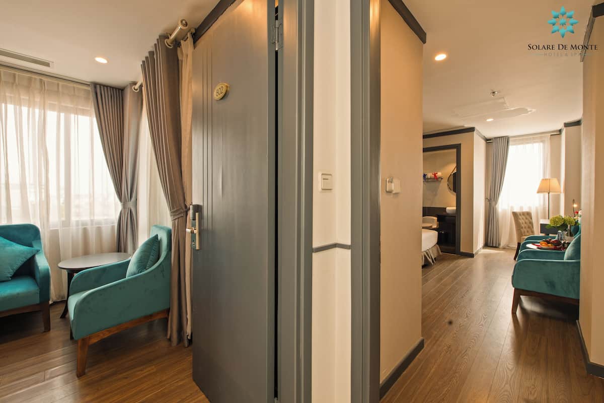 A hotel room with teal armchairs, a wooden floor, and a sliding door.