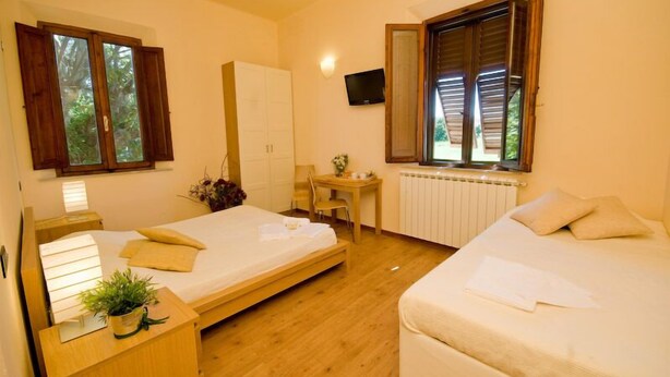 A room with two beds, a desk, a chair, a TV, and a window with shutters. - B&B Dolce Notte (Pisa)