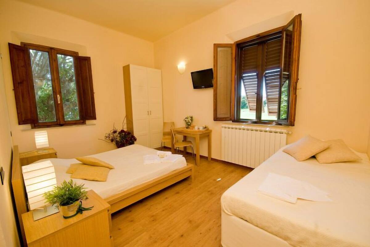 A room with two beds, a desk, a chair, a TV, and a window with shutters.