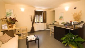 A modern living room with a sofa, a coffee table, a reception desk, and a window with blinds. - B&B Dolce Notte (Pisa)
