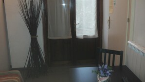 A room with a dining table, a chair, a vase with flowers, a broom, and a door with a curtain. - B&B Dolce Notte (Pisa)