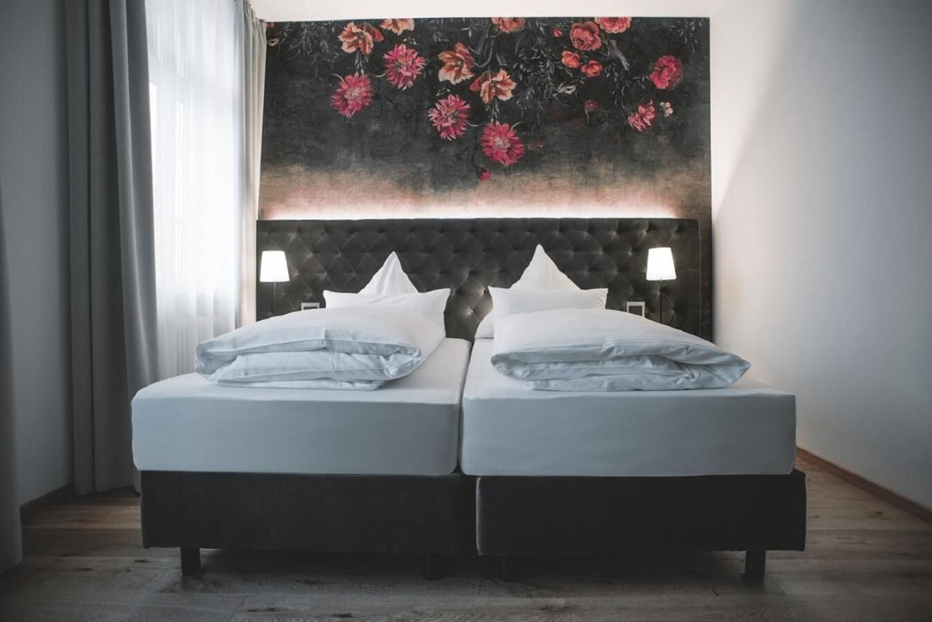 A double bed with a tufted headboard, two bedside lamps, and a floral artwork above.