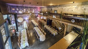 En rymlig restaurang med långa bord, hängande, sfäriska lampor och en rustik stenmur.