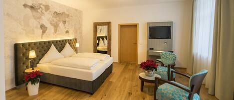 A hotel room with a large bed, a desk with a TV, and a seating area with chairs.