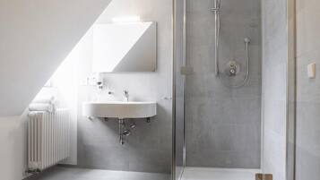 A modern bathroom with a glass-enclosed shower, a white sink, and a radiator.