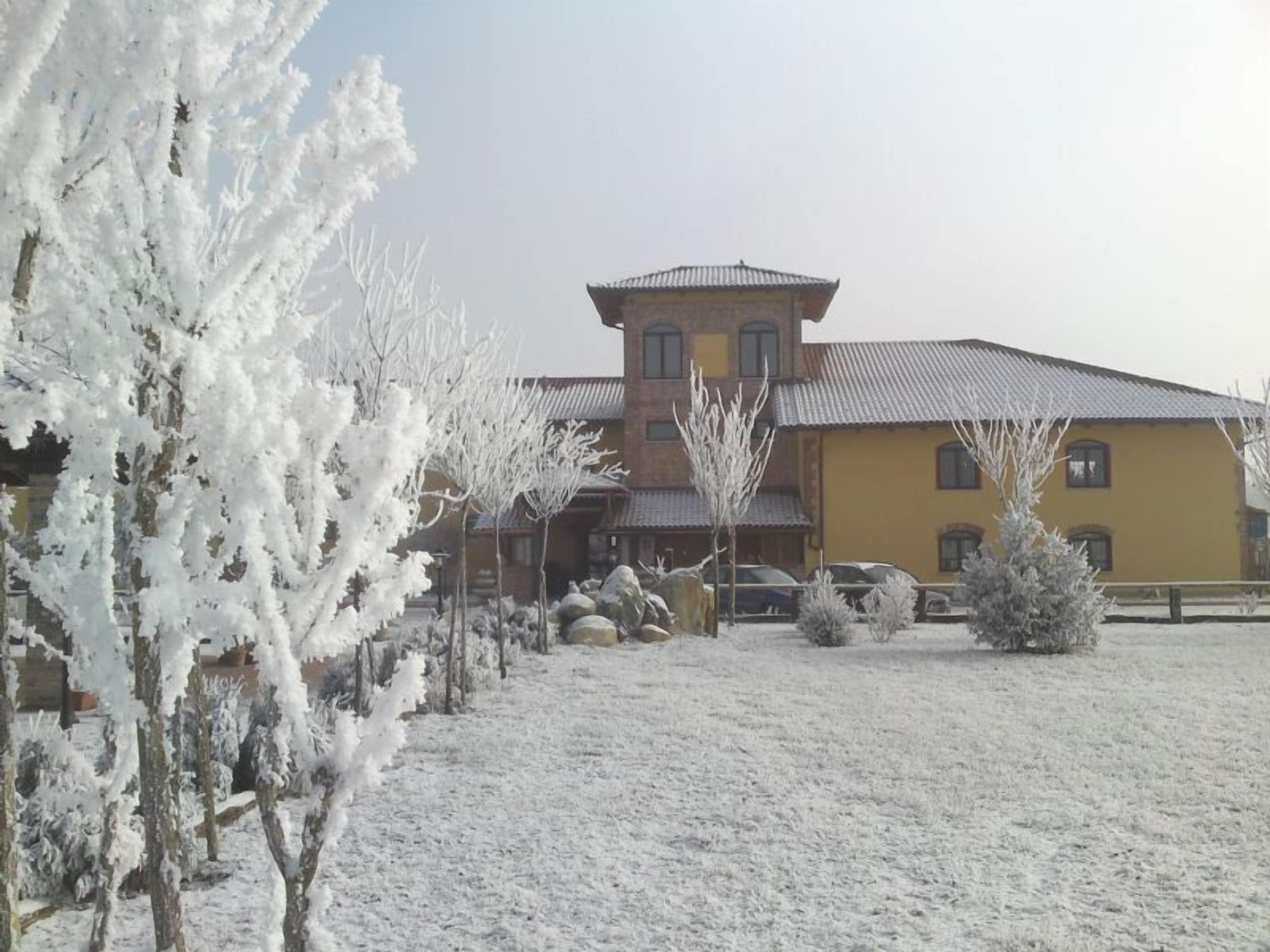 A two-story building with a yellow facade and a red roof, surrounded by snow-covered trees and a clear sky.