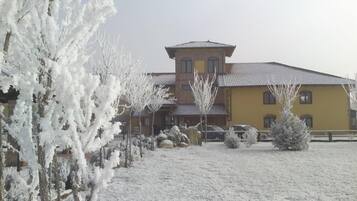 A two-story building with a yellow facade and a red roof, surrounded by snow-covered trees and a clear sky.