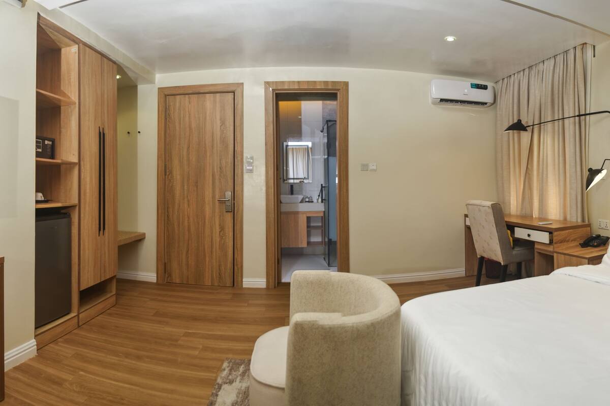 A hotel room with a bed, a desk with a chair, a wardrobe, and a kitchenette.