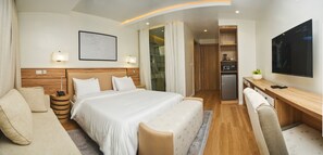 A hotel room with a large bed, a desk, a TV, and a shower area. - Centurion Apartments Limited (Abuja)