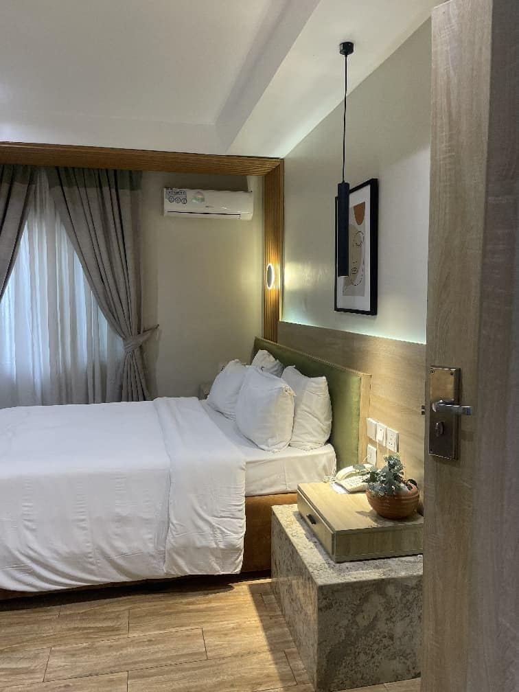 A hotel room with a bed, bedside table, and a wall-mounted air conditioning unit.