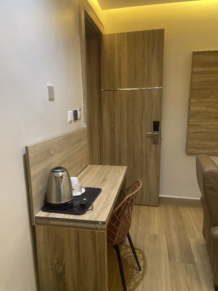 Ein kleines Zimmer mit einem Holztisch, einem Stuhl, einer Kaffeemaschine und einer Tür.