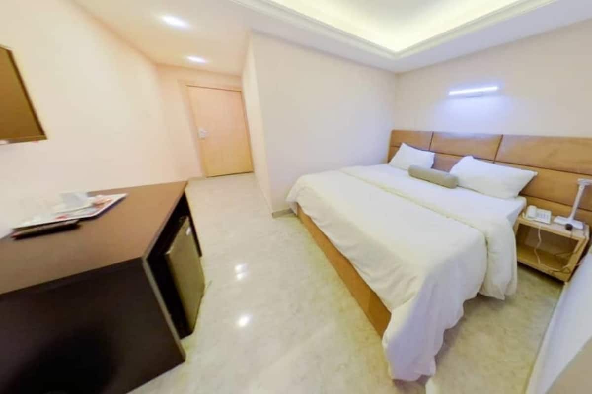 A hotel room with a bed, bedside table, lamp, and a desk with a chair.