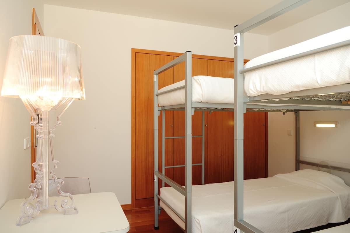 A bunk bed room with a wooden door, a table with a lamp, and a number sign on the wall.