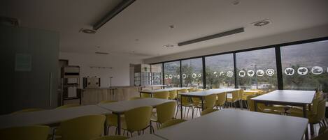 A dining area with tables and chairs, large windows with a view, and a ceiling with ventilation.