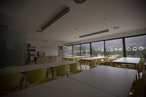 Un comedor con mesas y sillas, ventanas amplias con vistas, y un techo con ventilación.