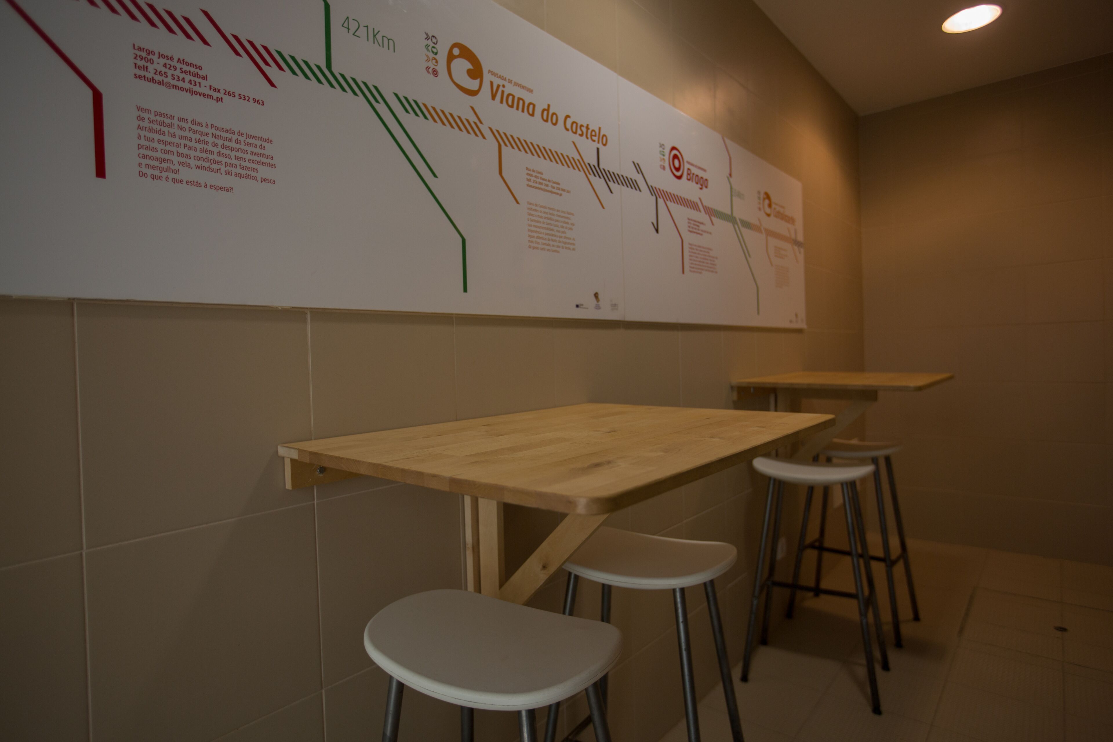 A restaurant interior with a long table and stools, a wall with a map and text, and tiled walls.