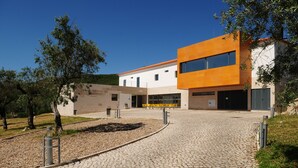 A modern building with a paved courtyard, outdoor seating, and trees. - HI Alvados - Pousada de Juventude - Hostel (Porto de Mos)