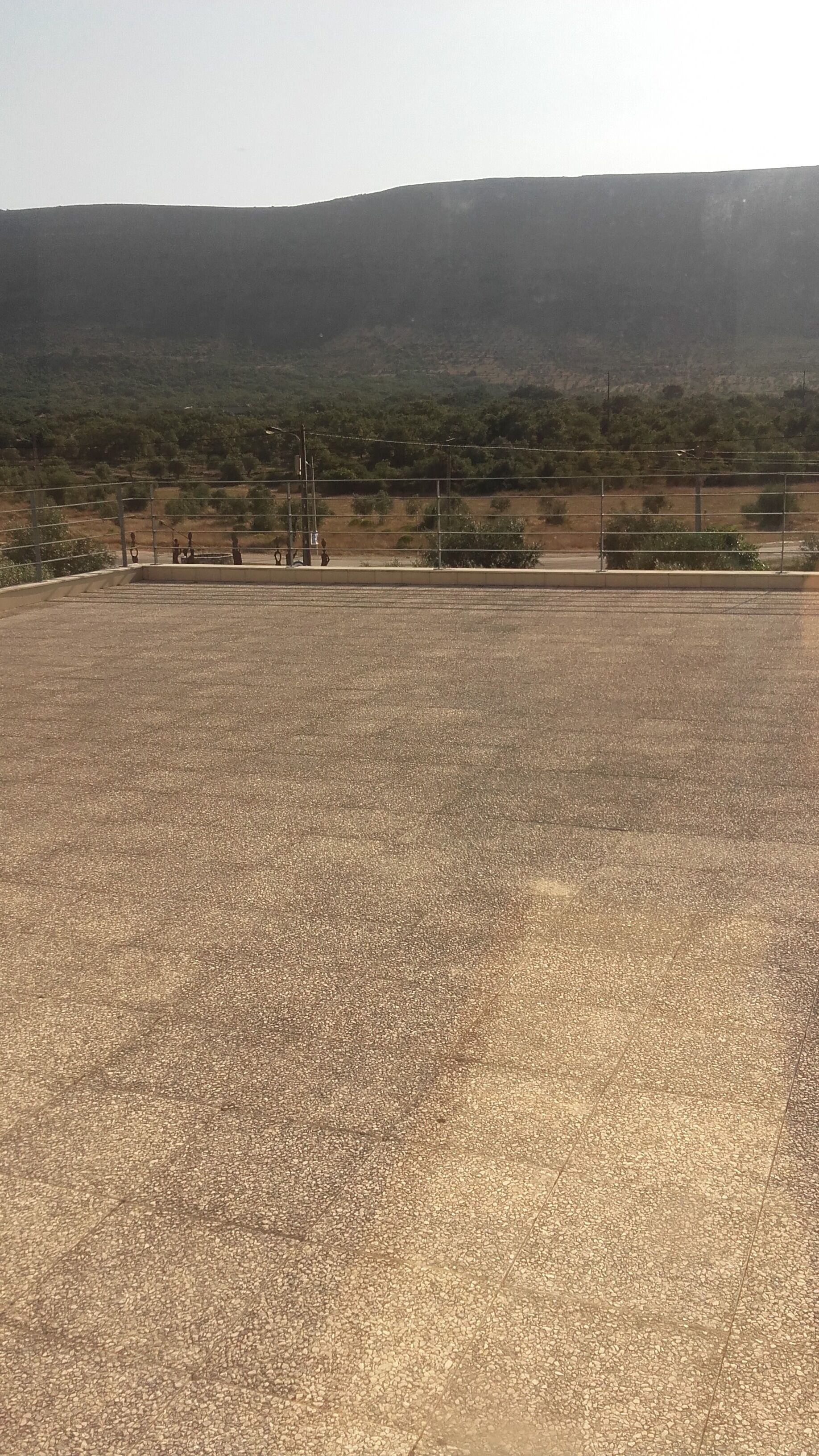 A large, open paved area with a metal fence and a hilly landscape in the background.