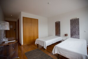 Habitación de hotel con dos camas individuales, un armario de madera, un escritorio con silla y una mesita con lámpara.