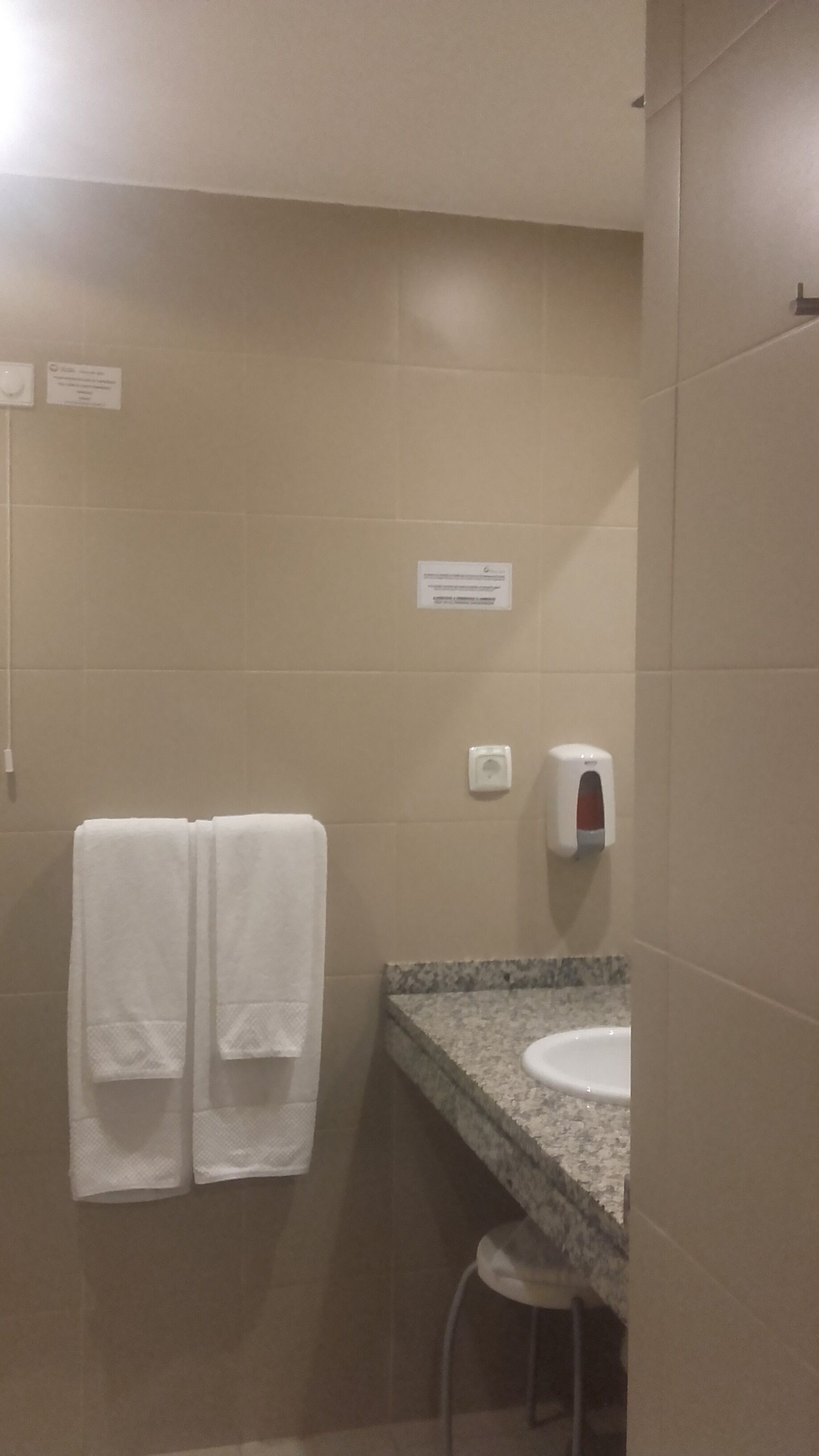Un baño con dos toallas blancas colgadas en una pared, un dispensador de jabón y un lavabo con encimera de granito.