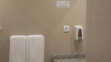 Un baño con dos toallas blancas colgadas en una pared, un dispensador de jabón y un lavabo con encimera de granito.