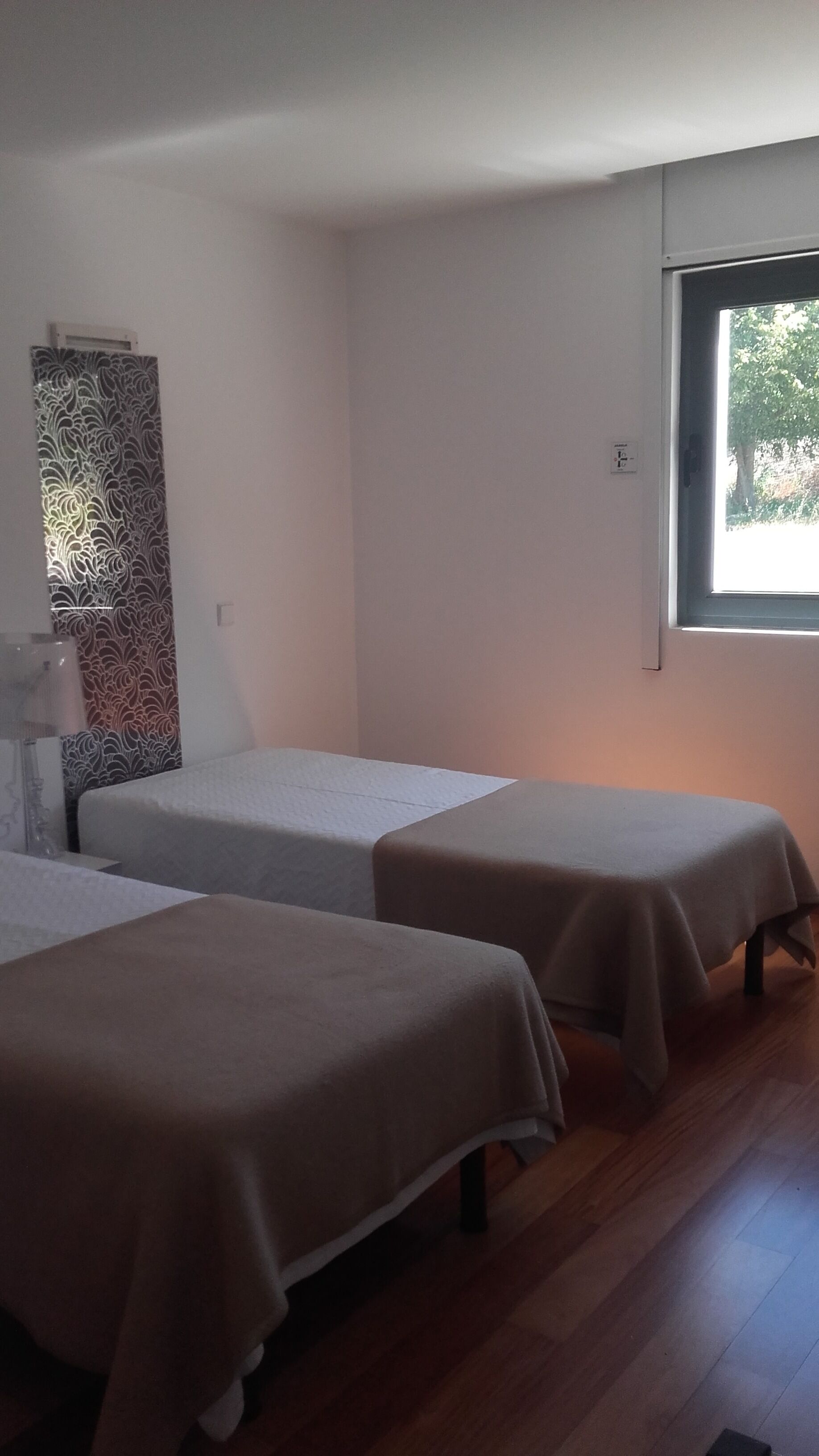 Una habitación con dos camas individuales, un adorno de pared con diseño y una ventana con vistas a árboles.