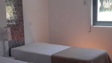 Una habitación con dos camas individuales, un adorno de pared con diseño y una ventana con vistas a árboles.